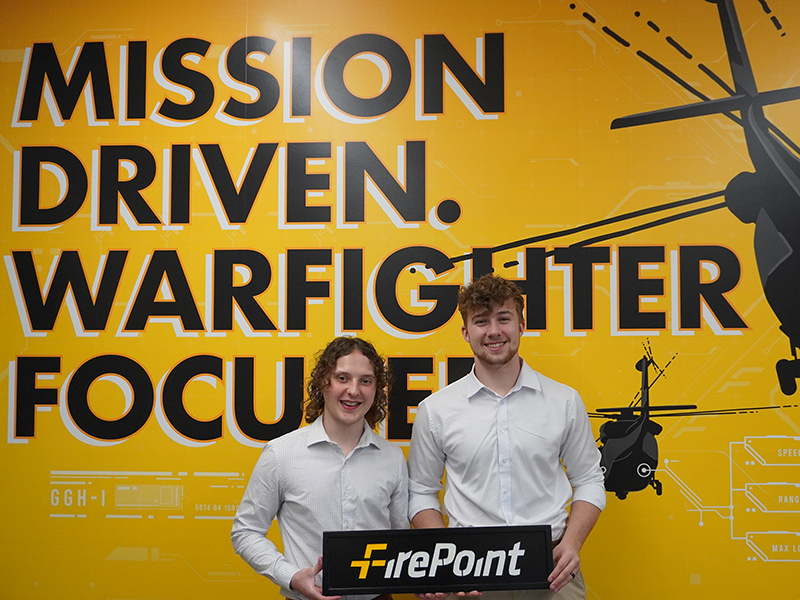 Greg Heiman and Murphy Ownbey hold a FireaPoint sign in front of a yellow background with black letters that spell out 